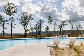 A pool surrounded by trees and chairs.